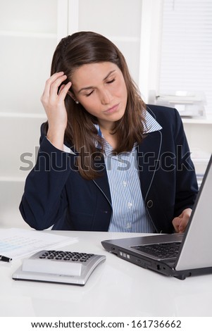 Burnout: overworked tired businesswoman in blue scratching head at desk with laptop and calculator