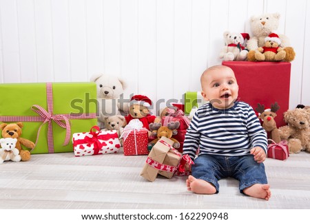 Christmas and birthday - cute baby sitting barefoot and looking excited surrounded by teddy bears and presents