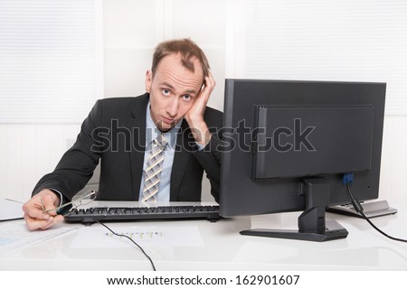 Frustrated employee sitting and desk holding his head - problems and stress at work