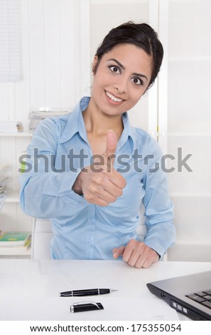 Successful smiling business woman with thumb up at desk at office.