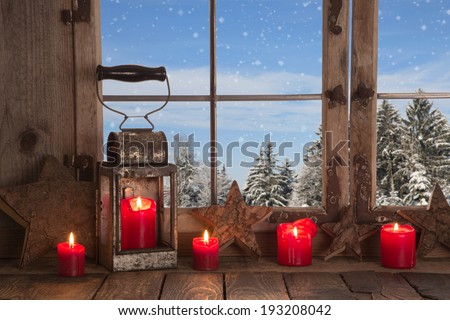 Country Christmas decoration: wooden window decorated with red candles and rustic lantern. View to the mountains in the alps.