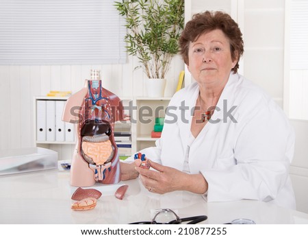 Portrait of happy older senior doctor or professor explaining the human body with a torso.
