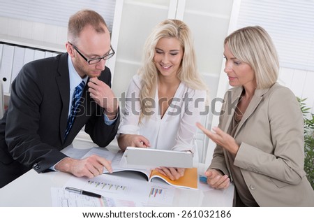 Business team of man and woman sitting around desk in a meeting looking at tablet.