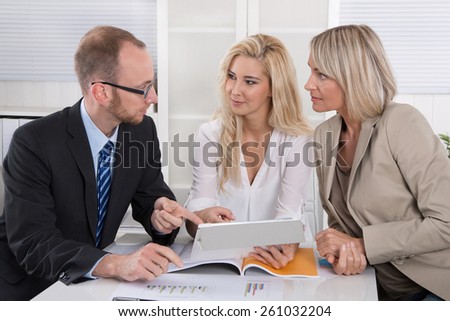 Business team of man and woman sitting around desk in a meeting looking at tablet.