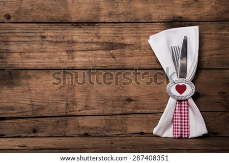 Lovely cutlery in red in white checked plus heart and napkin on old wooden background.