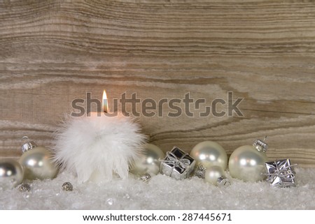 One burning candle with white feathers and snow and silver decoration on a wooden background for christmas.