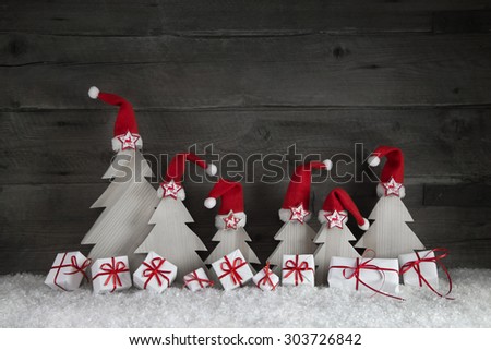 Funny christmas trees with santa hats and gift boxes on wooden background with red ribbon and snow for decoration.