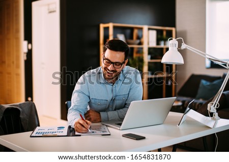 Photo of Young business man working at home with laptop and papers on desk