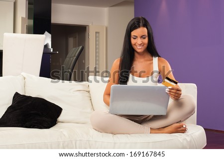 Young woman sitting on the sofa and  shopping online with credit card. Selective focus on face.