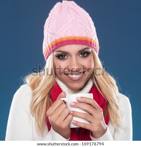 Beautiful young woman with winter cap and scarf around the neck holding teacup