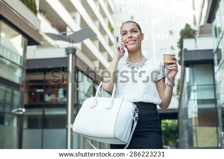 Young businesswoman holding coffee to go and talking on the phone