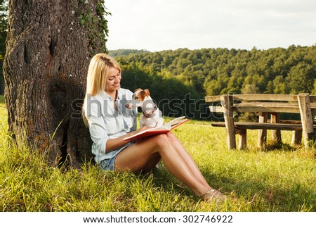 Young woman reading a book in the nature with her dog