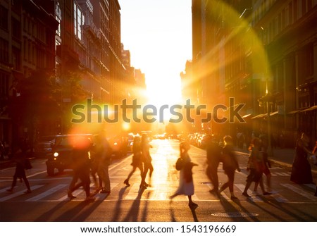 People walking across the street in New York City with the bright light of sunset shining between the buildings along 23rd St in Midtown Manhattan NYC