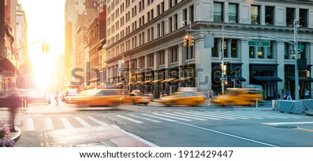 New York City - Busy intersection with yellow taxis speeding through the crowded intersection of 5th Avenue and 23rd Street with the light of sunset shining in the background