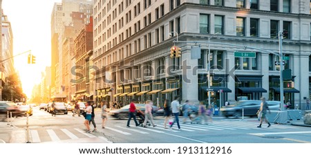 Crowds of people in motion walking across the busy intersection on 5th Avenue in Midtown Manhattan, New York City NYC
