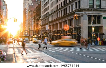 Busy New York City scene with crowds of people and cars in the intersection of Fifth Avenue and 23rd Street in Midtown Manhattan with the light of sunset in the background