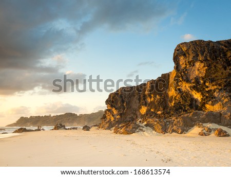 Large sea cliffs at sunrise with white sand and two motion blurred people fishing