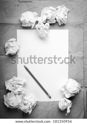 Writing concept - crumpled up paper wads with a sheet of white paper and pencil in black and white