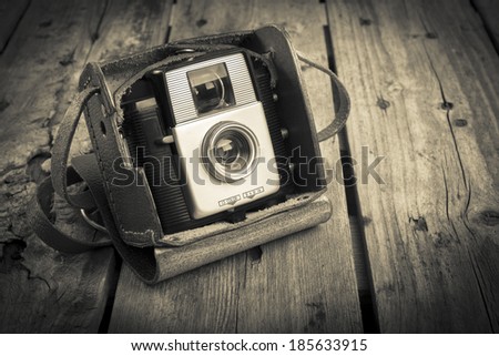 An old camera in its original vintage leather case on a wooden background filtered