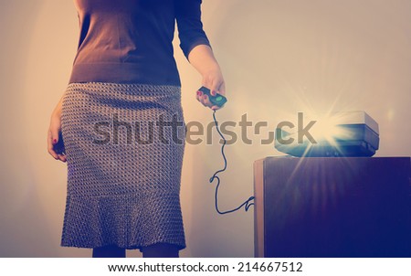 Retro styled woman operating a slide projector with a wired remote control and lens flare from projector light
