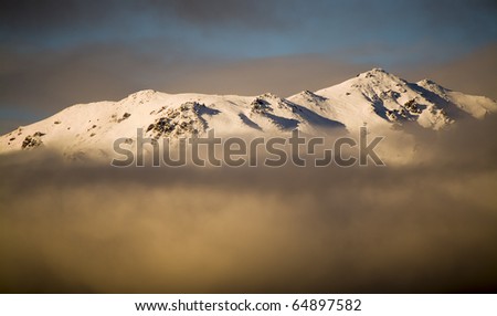 South Island, New Zealand. The tip of a mountain peaks through the clouds.