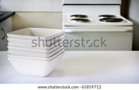 Contemporary square white bowls sit on the kitchen bench with stove behind
