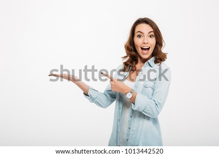 Photo of Photo of happy young woman standing isolated over white wall background. Looking camera showing copyspace pointing.
