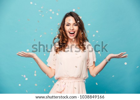 Portrait of a cheerful beautiful girl wearing dress standing standing under confetti rain and celebrating isolated over blue background 商業照片 © 