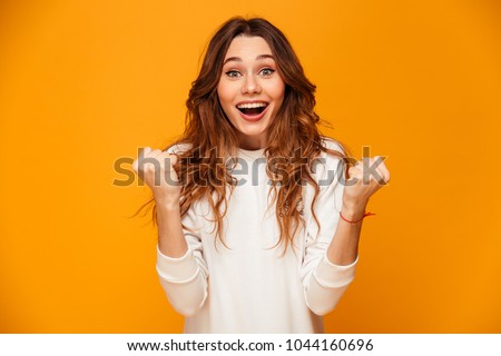 Surprised happy brunette woman in sweater rejoices and looking at the camera over yellow background Stockfoto © 