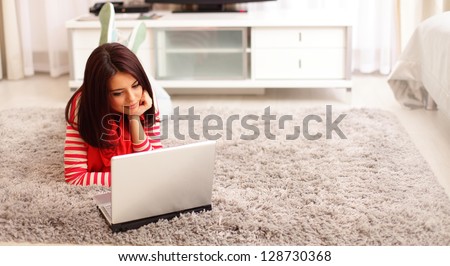 Portrait of dreamy smiling young woman using laptop while lying on floor at home