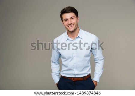Image of happy brunette man wearing formal clothes smiling at camera with hands in pockets isolated over gray background Stock foto © 