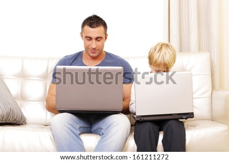 Father and son working on their computers on the sofa at home