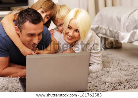 happy family lying on the carpet and playing on a laptop at home