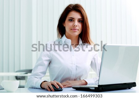 Young serious businesswoman sitting at the table with laptop in office
