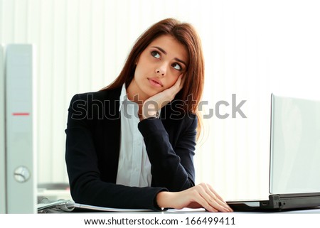 Young pensive businesswoman looking away at copyspace in office