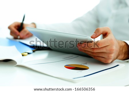 Closeup image of a man holding tablet computer and writing something down