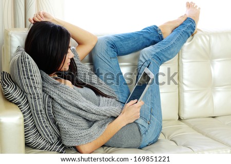 Young beautiful woman resting on a sofa with tablet computer at home