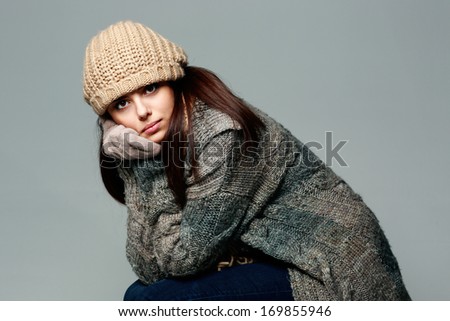 Young pensive woman in warm winter outfit on gray background