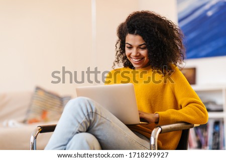 Image of cheerful african american woman using laptop while sitting on chair in living room ストックフォト © 