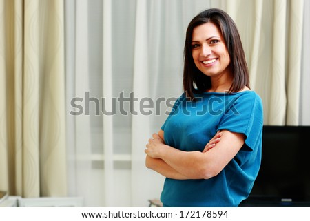 Young happy smiling woman standing with arms folded at home