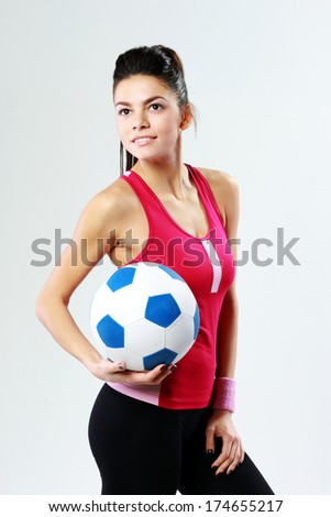 Young smiling sport woman holding a soccer ball on gray background