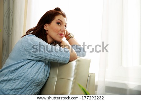 Thoughtful woman sitting on the sofa and looking up at home
