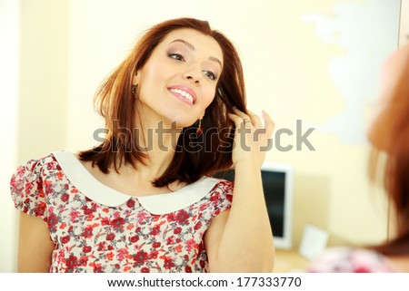 Smiling woman looking on her reflection in the mirror at home