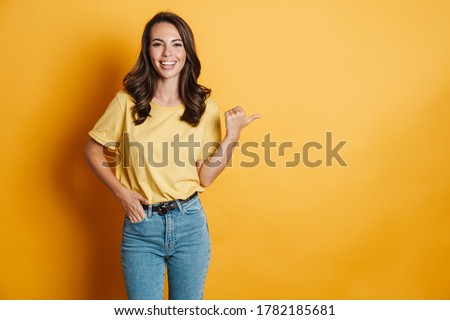 Image of joyful charming woman smiling and pointing finger aside isolated over yellow background