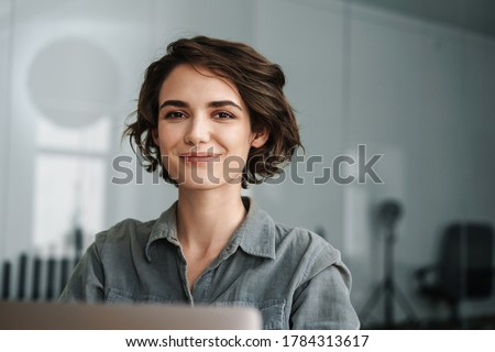 Photo of Image of young beautiful joyful woman smiling while working with laptop in office