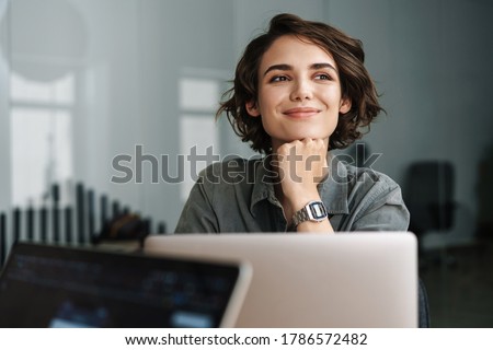 Image of young beautiful joyful woman smiling while working with laptop in office Foto stock © 