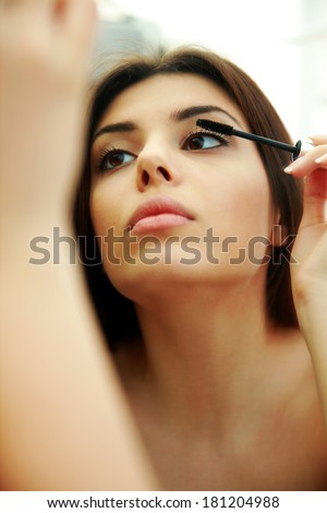 Young beautiful woman looking at mirror while doing makeup