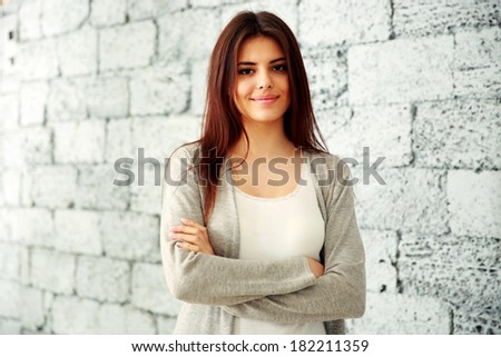 Young happy woman with arms folded standing near brick wall