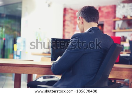 Back view portrait of a businessman sitting with laptop at office