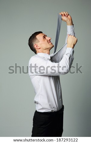 Businessman in suit hanging himself on tie on gray background